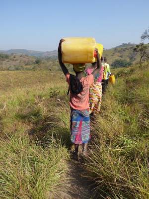 Frau in Afrika trägt gelben Wasserkanister in Steppenlandschaft